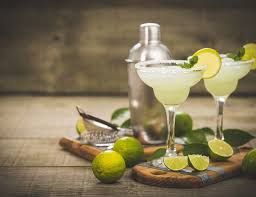 margaritas surrounded by limes and shaker